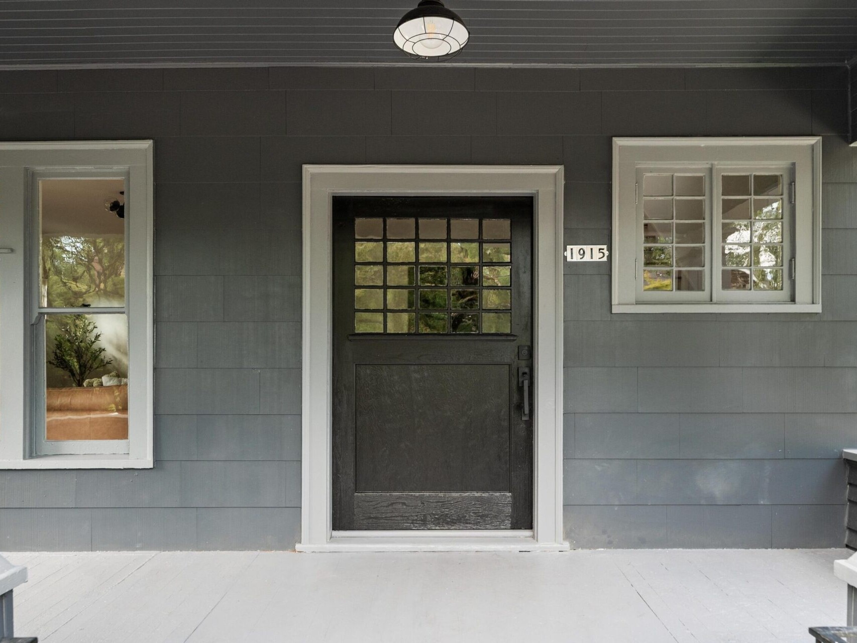 The front view of this Portland, Oregon home showcases a black door with grid-patterned windows, flanked by multi-pane windows. The house number 1915 graces the right side. Its dark gray exterior is elegantly highlighted with white trim.