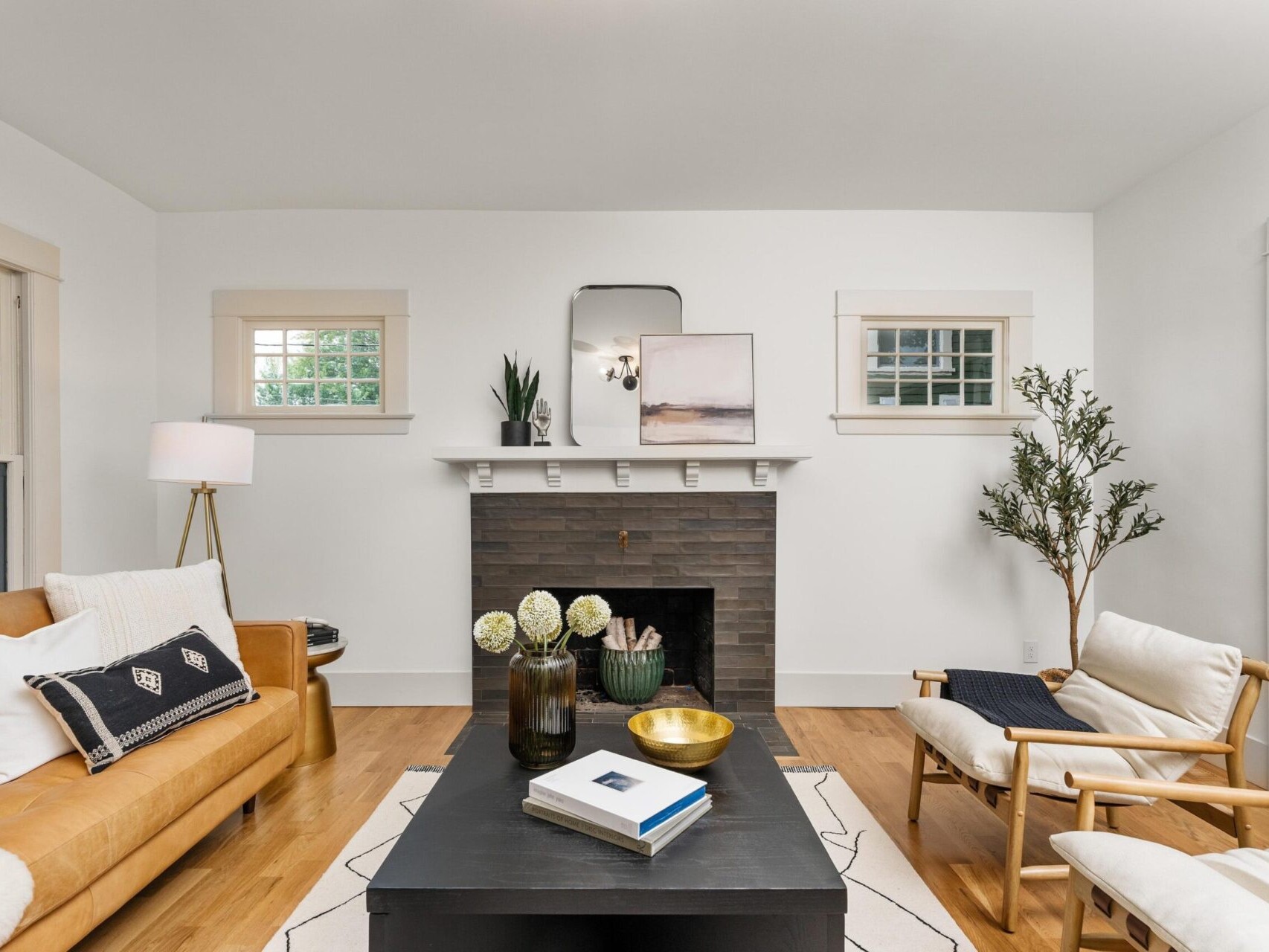 A cozy Portland, Oregon living room with a brown leather sofa, two chairs, and a black coffee table. The fireplace is adorned with a mirror and decor. A tall plant stands in the corner, and a floor lamp provides additional lighting. The wooden floor adds warmth.