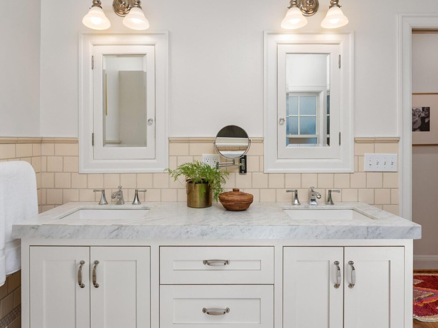 A Portland Realtor’s dream, this bathroom boasts a double vanity with white cabinets and a marble countertop. Two mirrors and wall sconces enhance the elegance, while a potted plant adds charm. Light tile and hardwood flooring complete this stunning space in the heart of Portland Oregon Real Estate.
