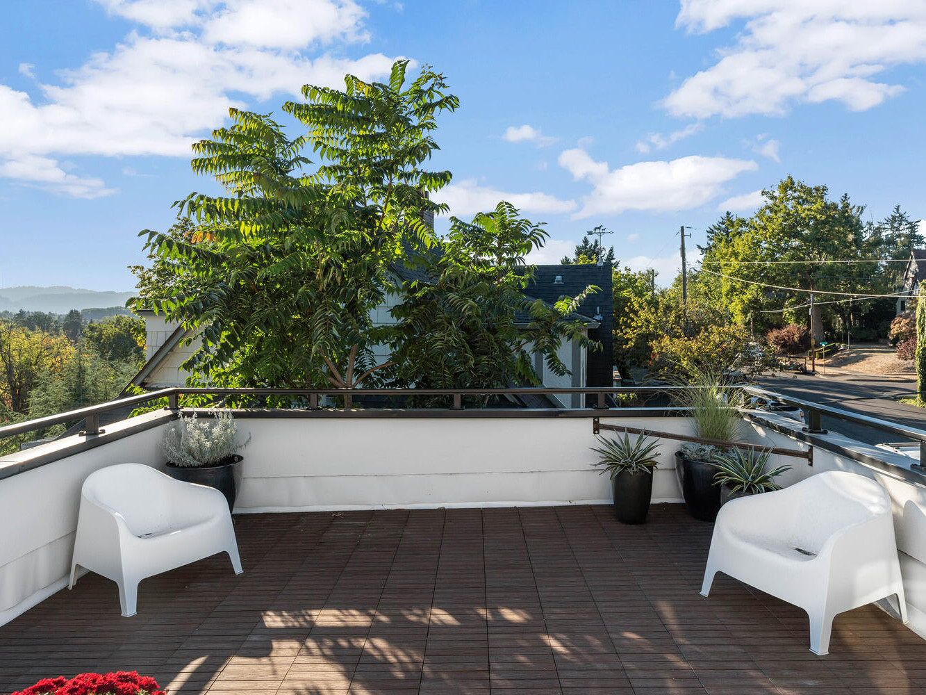 Rooftop patio in Portland, Oregon, with two white chairs and potted plants, overlooking a scenic view of trees and distant hills under a blue sky with clouds.