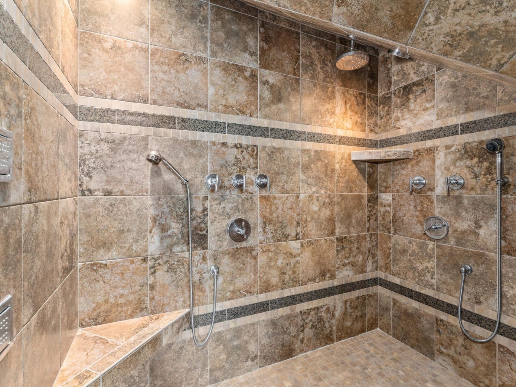 Experience luxurious showers in this Portland Oregon real estate gem, featuring brown stone tiles, dual rainfall showerheads, and handheld sprayers. A built-in corner bench and wall shelf for toiletries add functionality and elegance.