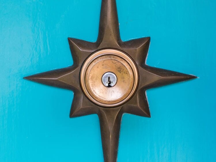 A brass star-shaped door knob with a central keyhole graces the vibrant turquoise doors of a charming Portland, Oregon home. The design elegantly features eight pointed rays extending from the circular center, adding a touch of flair to this unique urban abode.