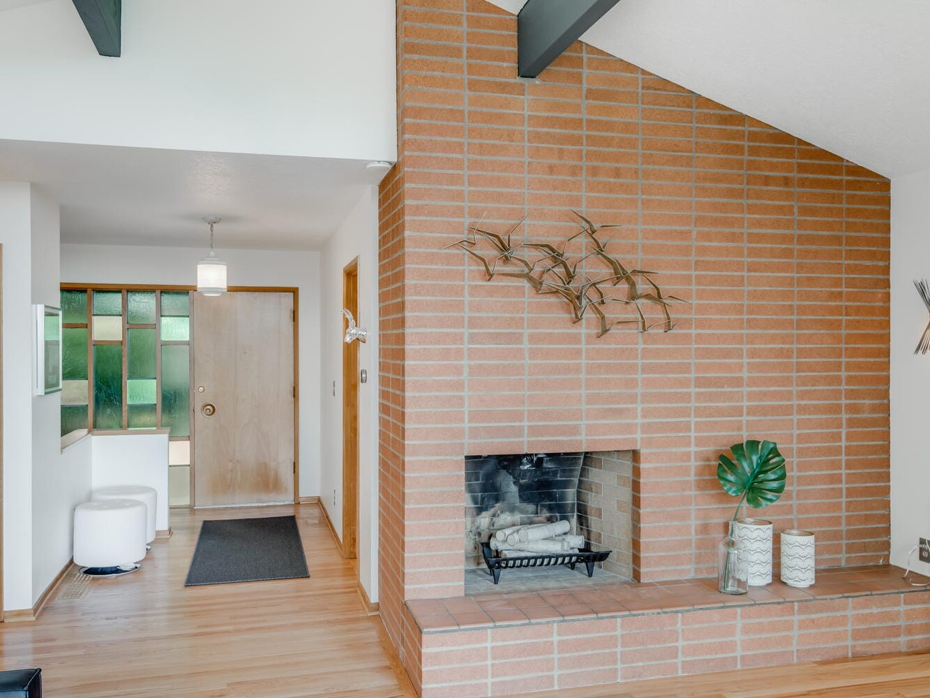 An interior space in Portland, Oregon, showcases a mid-century modern brick fireplace adorned with bird sculptures. To the right are decorative vases and a leaf, while in the background, a hallway features a wooden door and a small window.