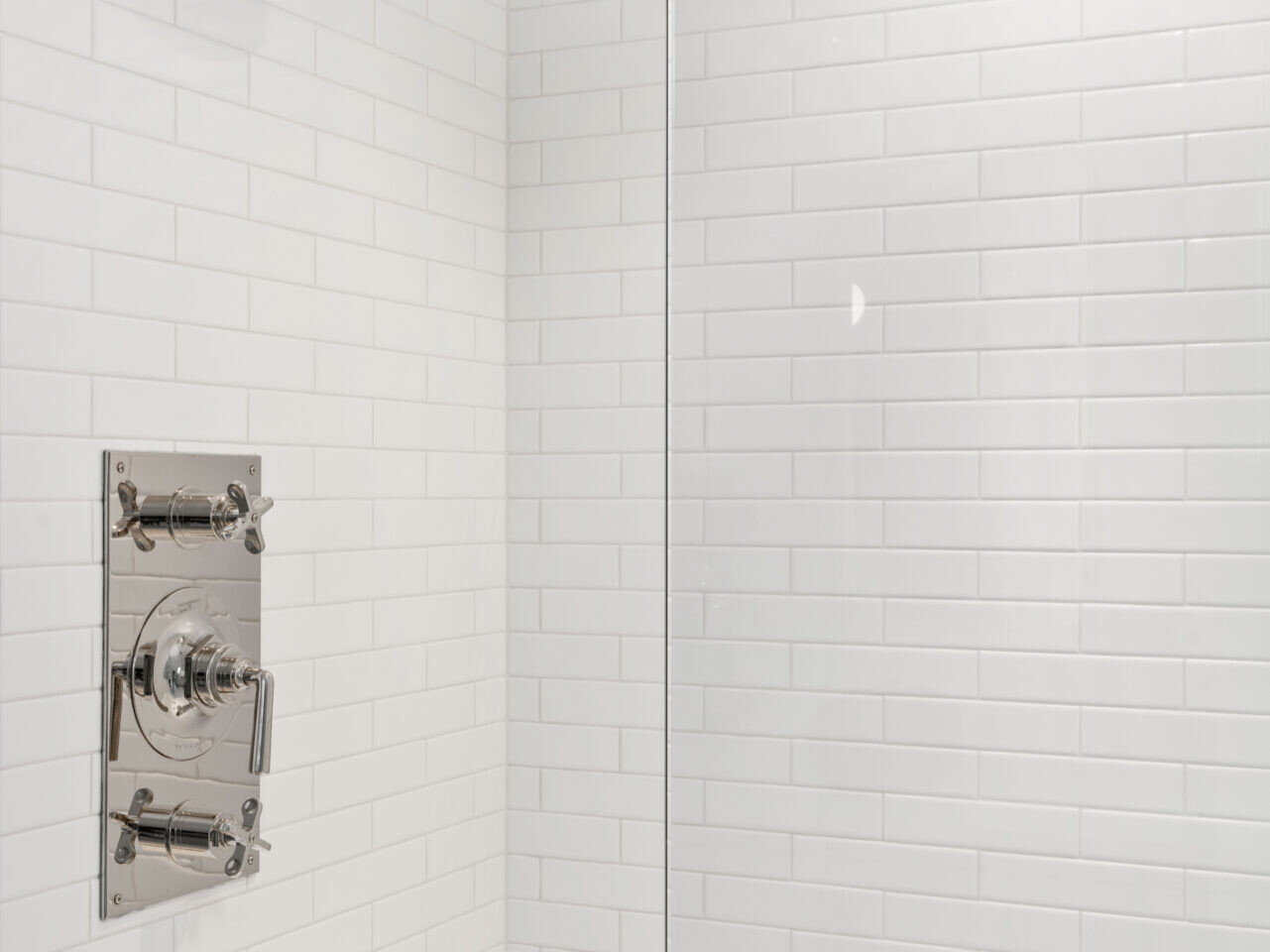 A modern shower in Portland, Oregon features white subway tile walls, a chrome-finished showerhead, and a square control panel. A rain showerhead descends from the ceiling, with a sleek glass partition visible on the right.