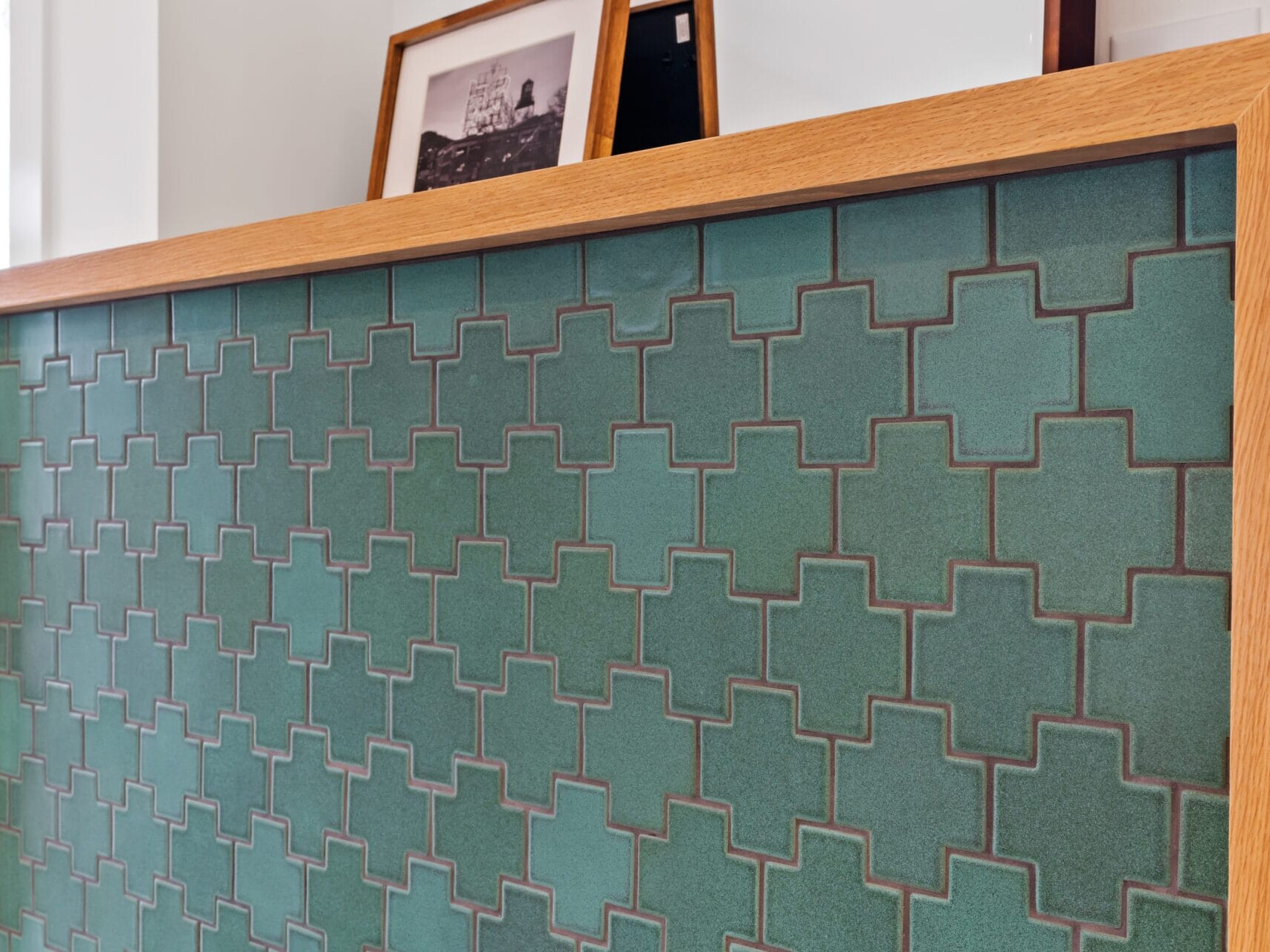 A wooden-framed wall panel with a geometric green tile pattern captures the essence of Portland, Oregon. On top of the panel, a few framed black-and-white photographs lean against the wall, adding an artistic touch to this modern space.