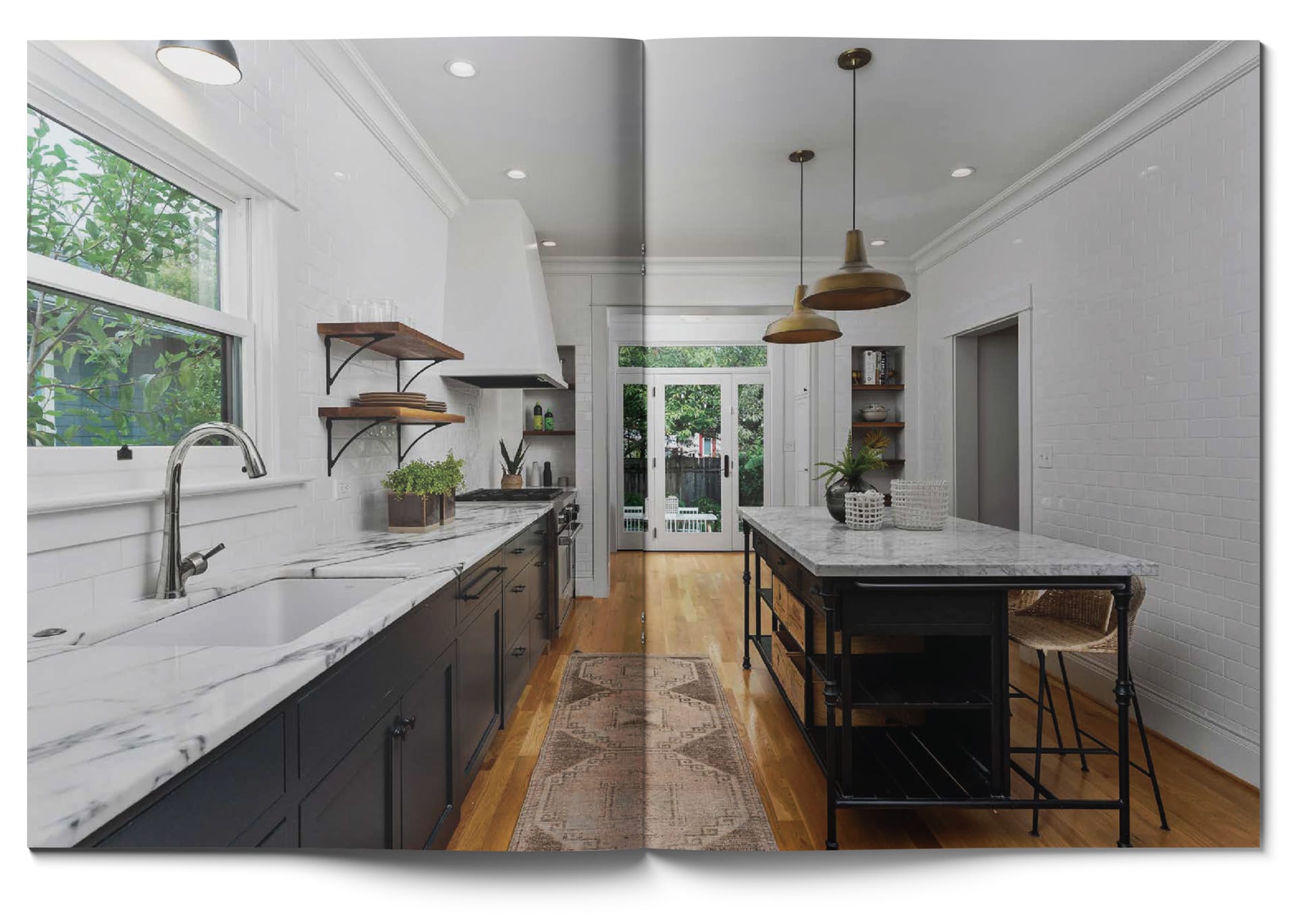 A modern kitchen with white walls and a marble countertop. Dark cabinets line both sides, with a large island in the center. Pendant lights hang above, and a window and glass doors offer views of greenery outside. A patterned rug lies on the wooden floor.