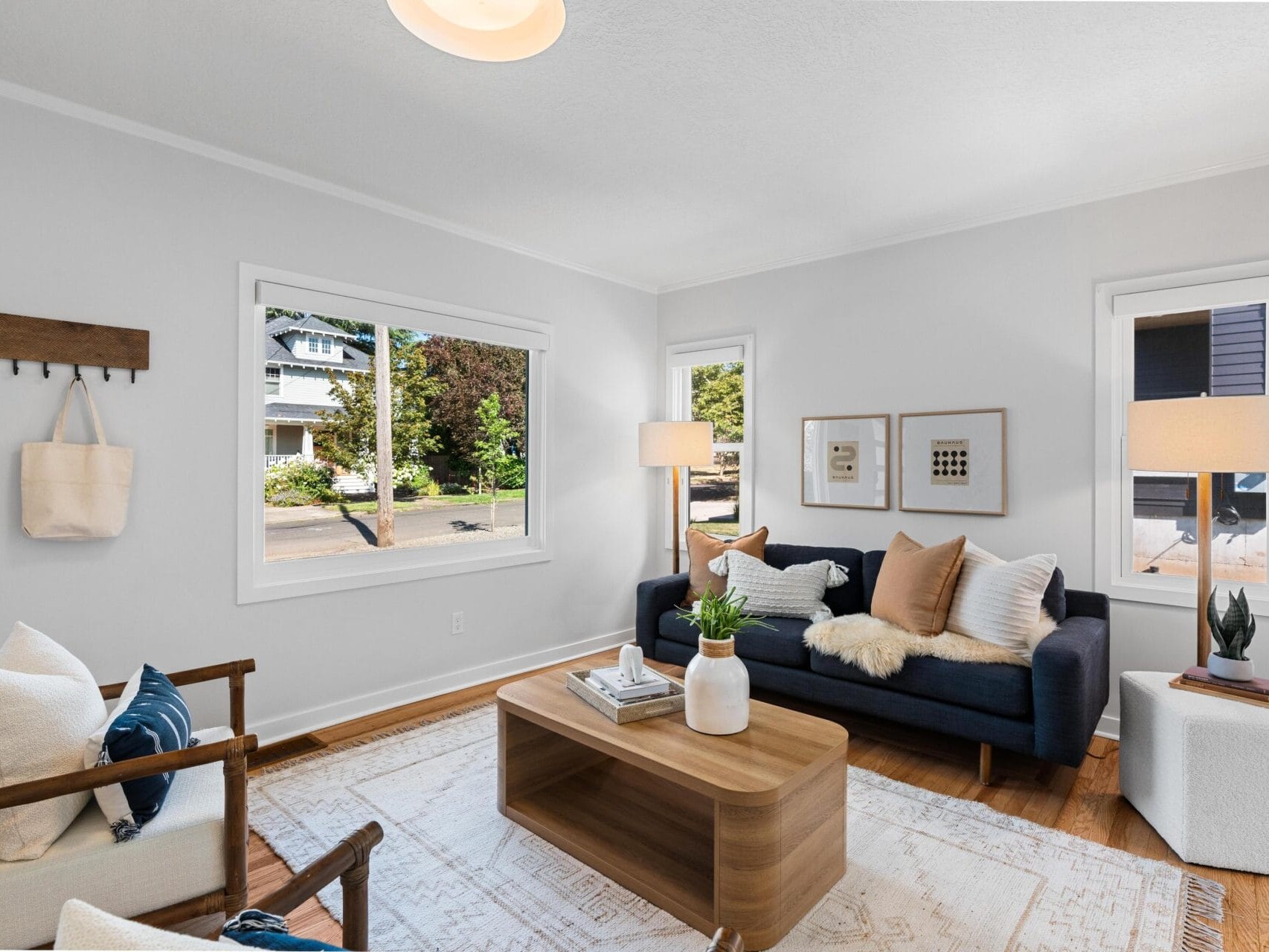 Bright living room with a navy sofa, two armchairs, a wooden coffee table, potted plants, and neutral decor. Large windows let in natural light, and light-colored walls enhance the airy atmosphere.