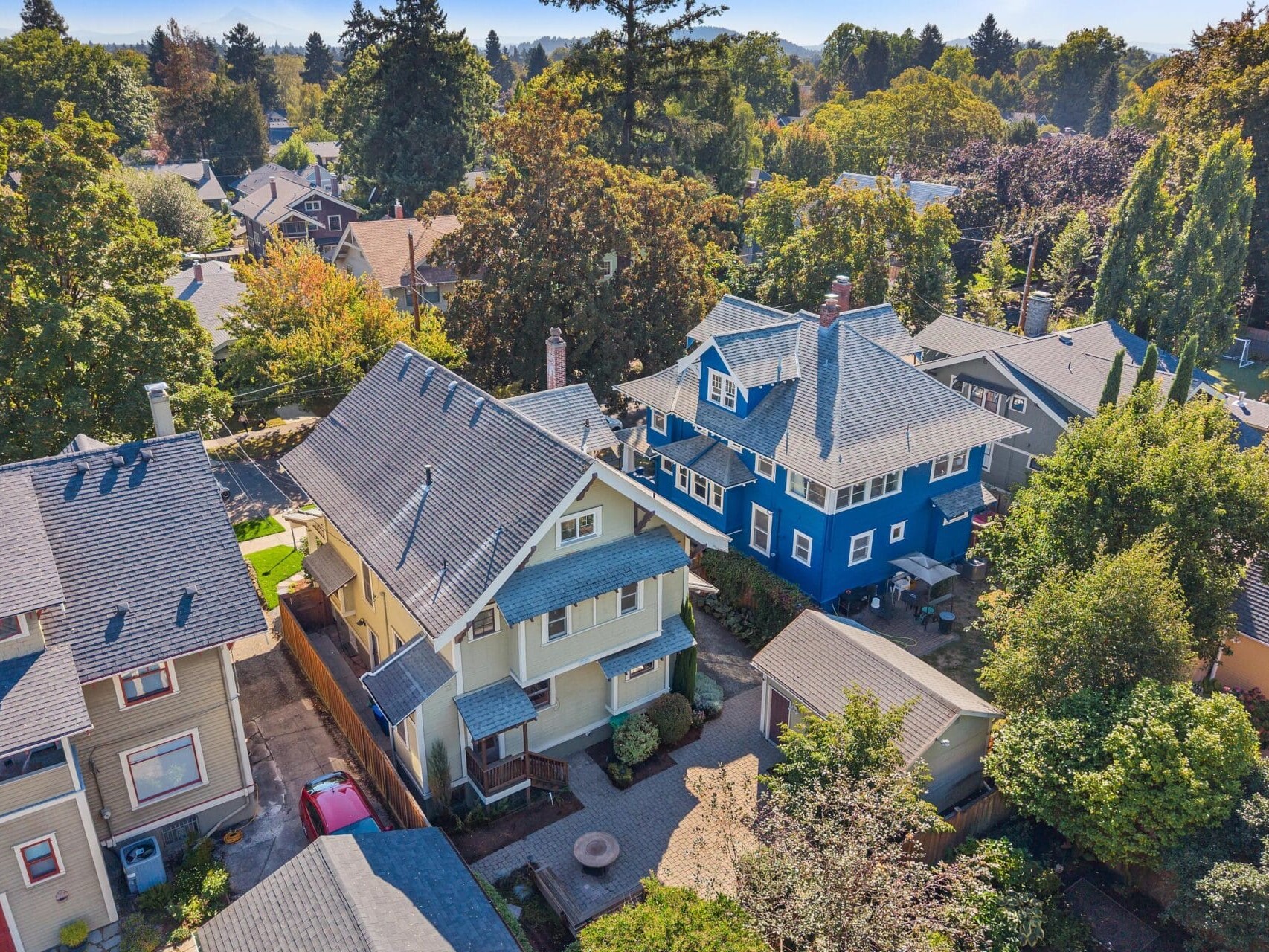 Aerial view of a residential neighborhood with tree-lined streets and houses in various colors, including a prominent blue house and beige homes surrounded by greenery.