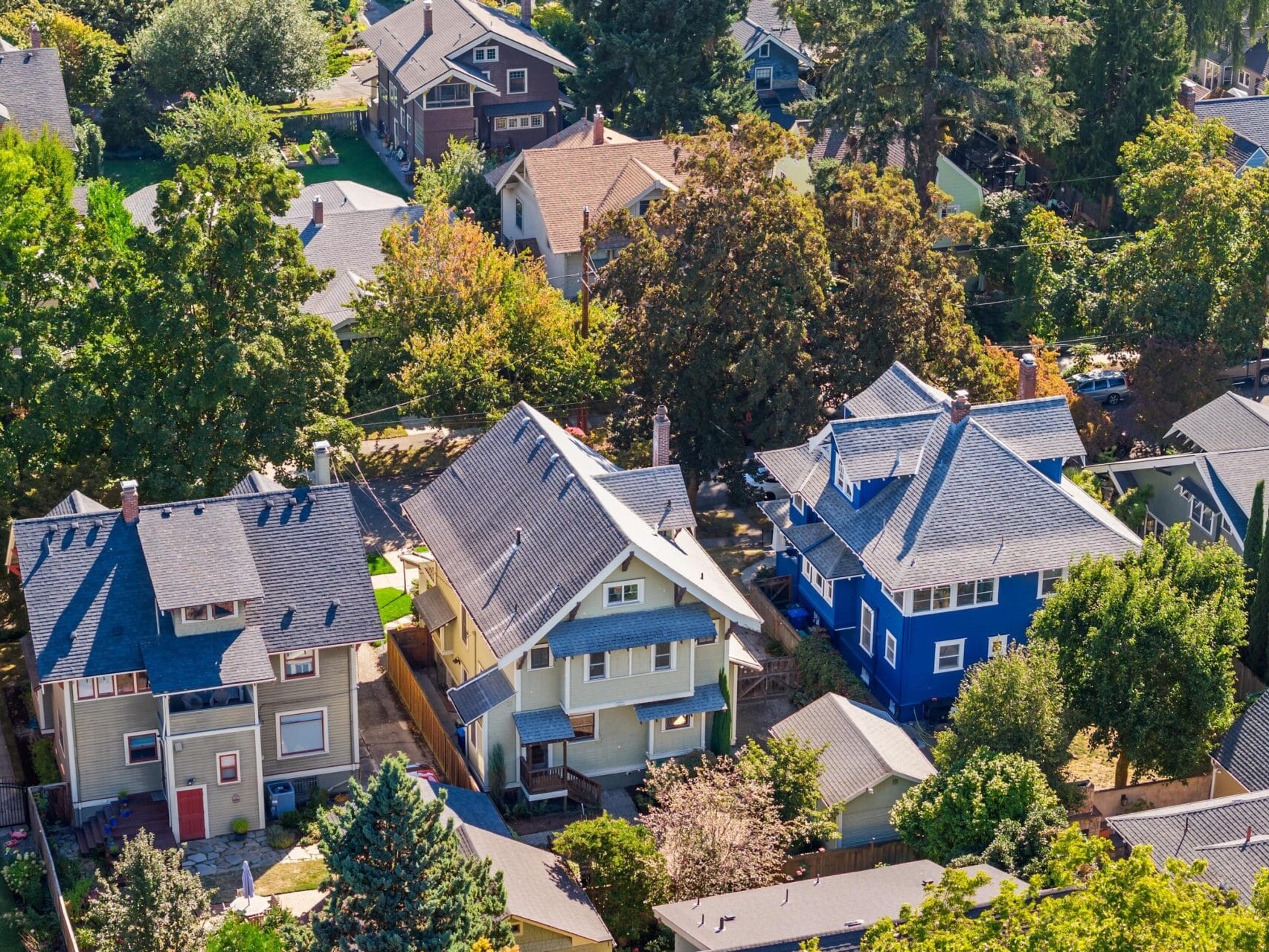 Aerial view of a suburban neighborhood with several colorful houses surrounded by trees and greenery on a sunny day.