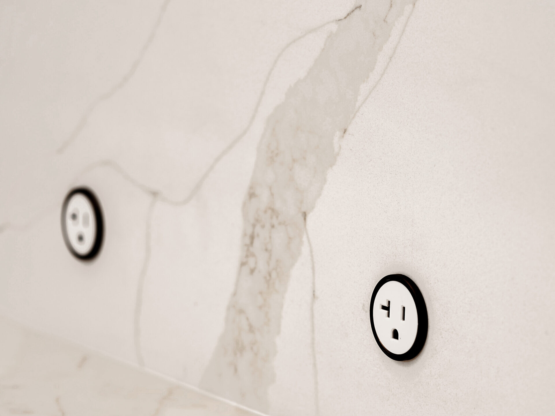 Two white electrical outlets with black rings are mounted on a marble backsplash with gray veining, matching the surface of the countertop below.