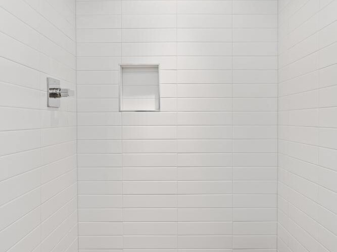 A modern shower with white tiled walls, a built-in shower niche, a chrome showerhead, and a brown tiled floor with a central drain under a recessed ceiling light.
