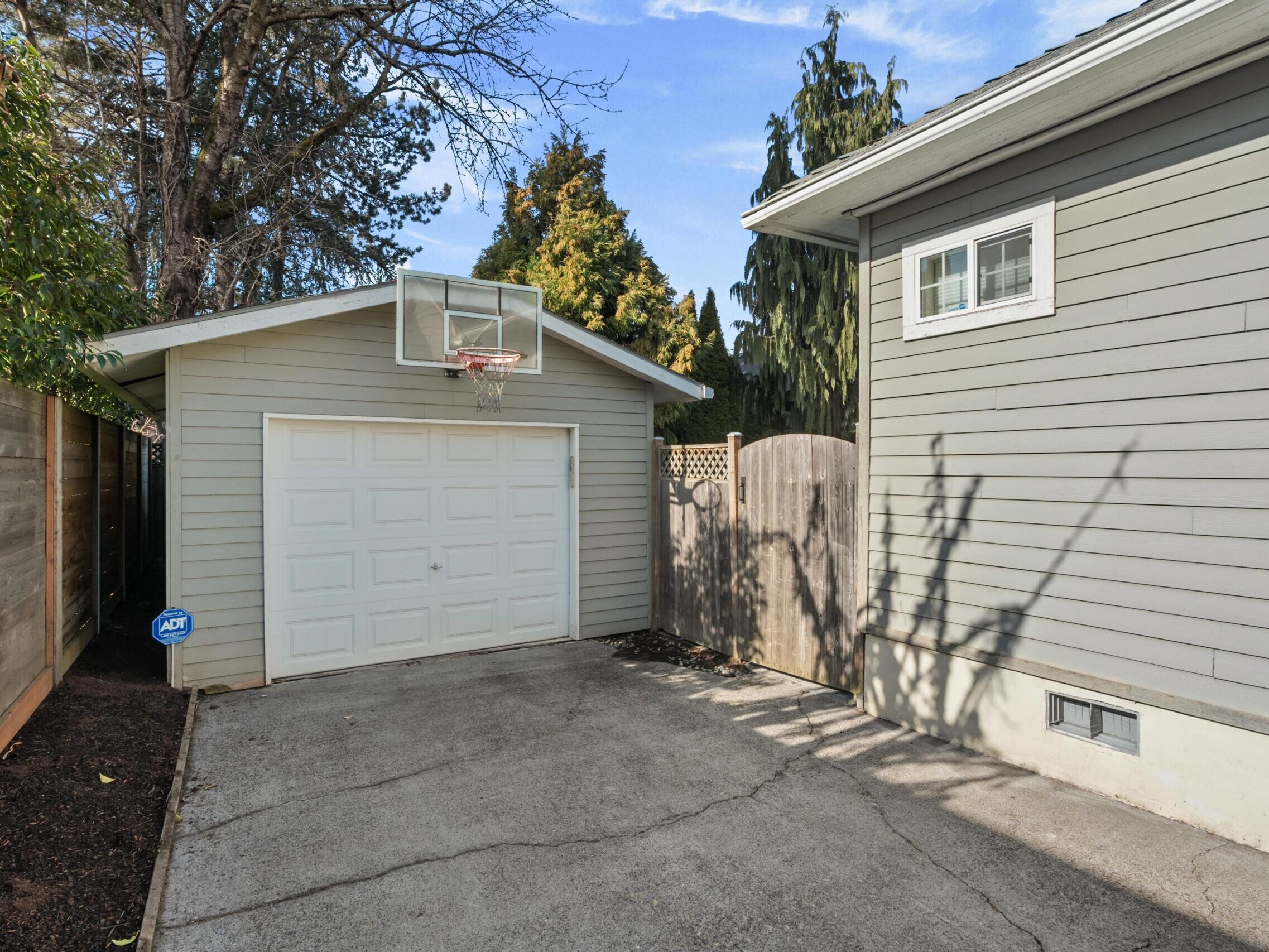 A garage with a basketball hoop in the back yard of a house.