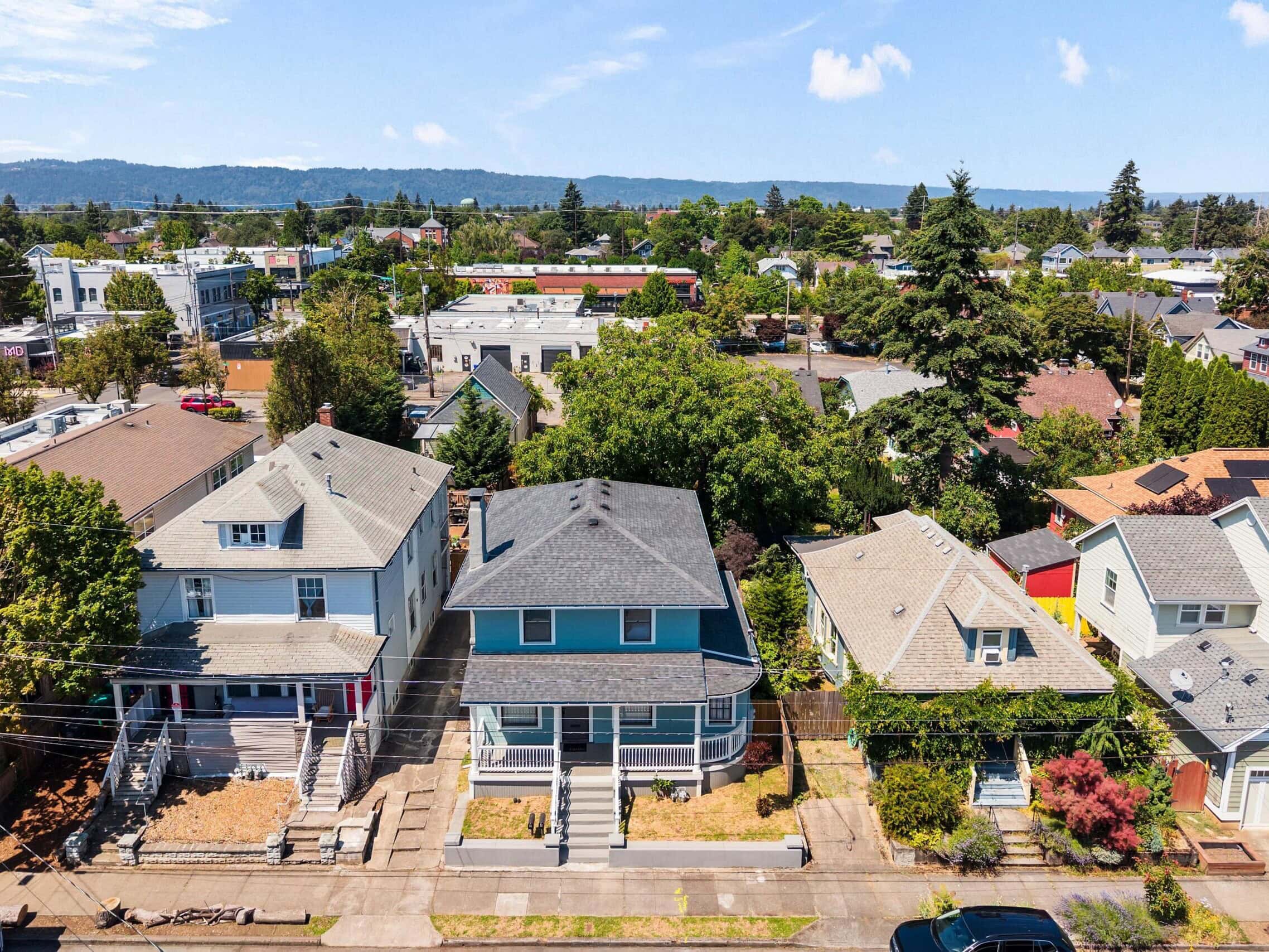 Aerial view of a suburban neighborhood with houses, trees, and streets under a blue sky with scattered clouds.