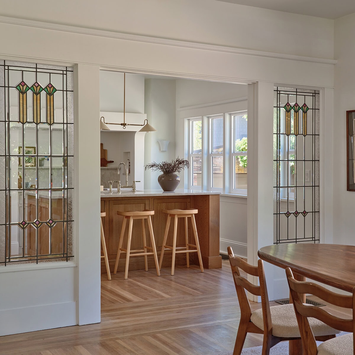 A view through a wide doorway into a kitchen featuring a wooden island with three stools, flanked by two built-in panels of stained glass, as seen in a listing by top real estate agent Portland Jim Arnal.