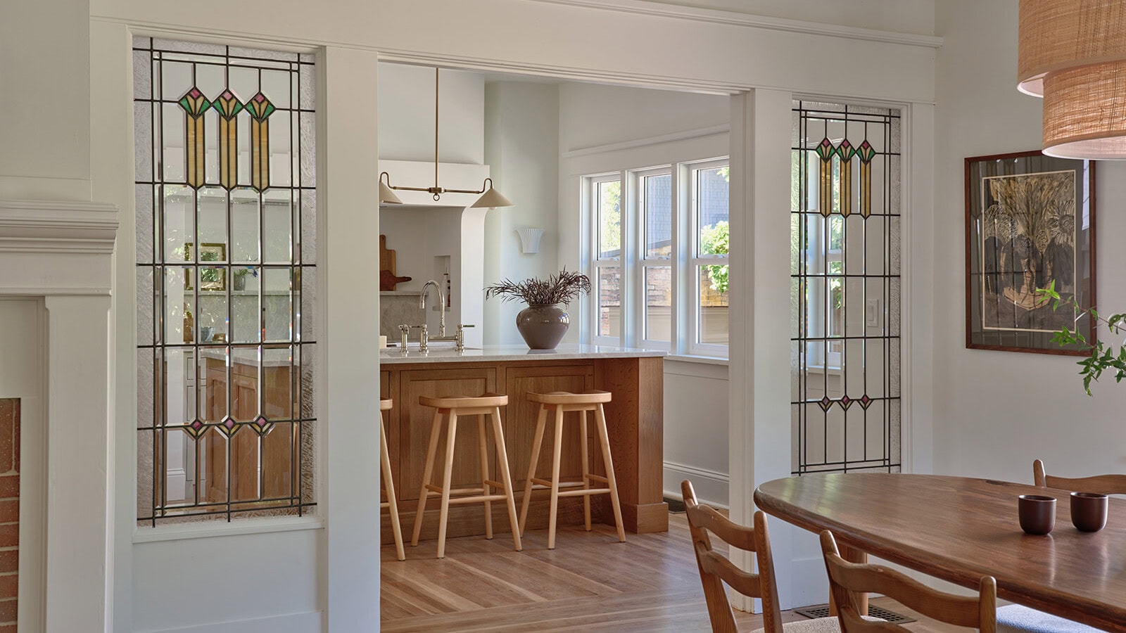 A view through a wide doorway into a kitchen featuring a wooden island with three stools, flanked by two built-in panels of stained glass, as seen in a listing by top real estate agent Portland Jim Arnal.
