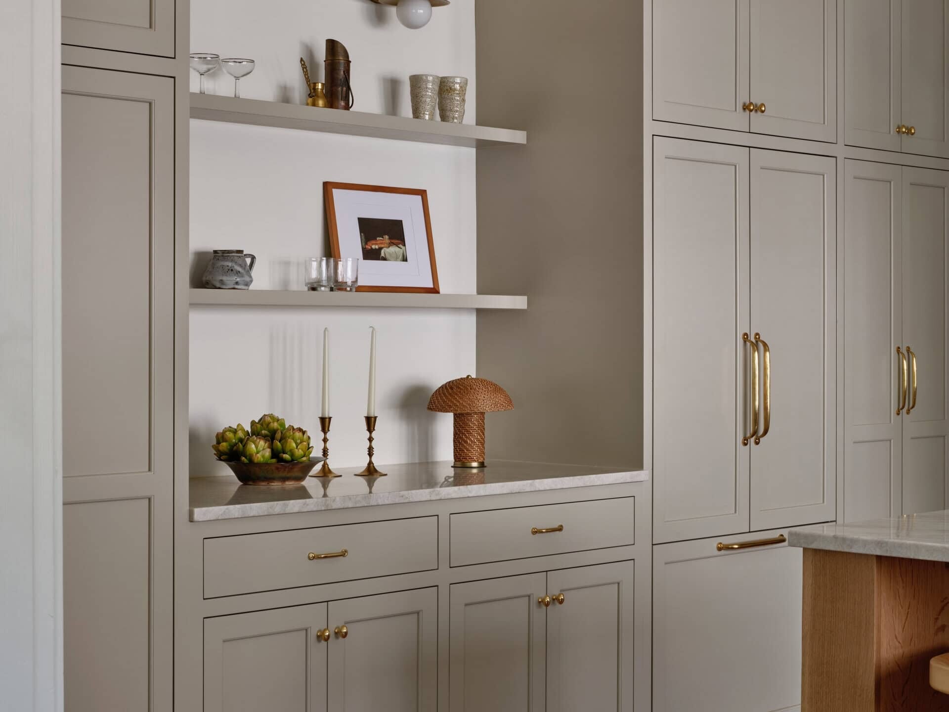Beige kitchen cabinetry with integrated appliances, open shelving styled with decor, and a marble countertop.