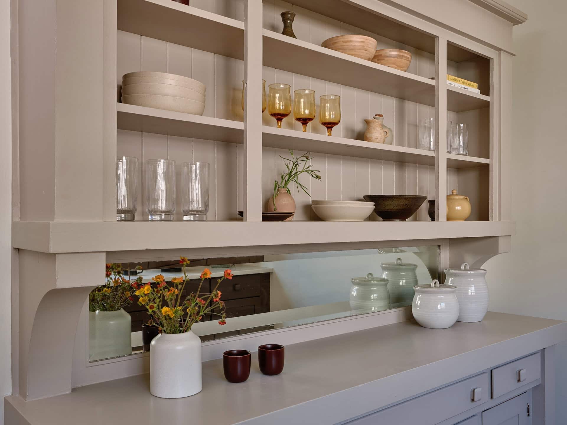 A built-in gray hutch filled with assorted glassware, bowls, and canisters, with a small vase of flowers sitting on the counter.