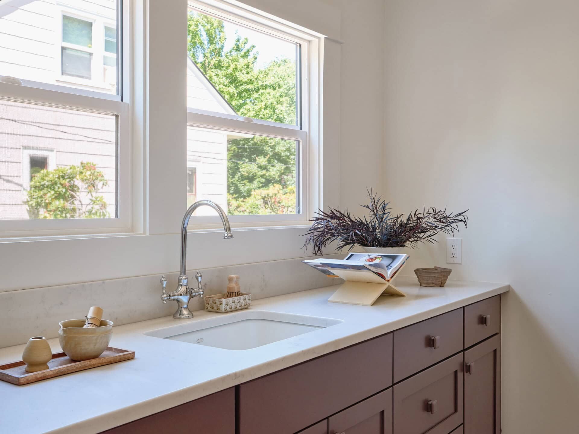 A kitchen counter with a sink, faucet, a mortar and pestle on a wooden tray, and a cookbook on a stand.